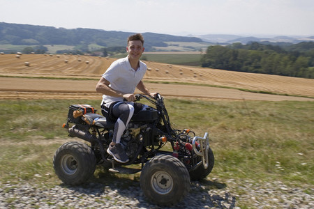 Portrait happy teenage boy riding quadbike in sunny rural field