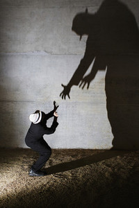 Man cowering from tall ominous shadow on wall