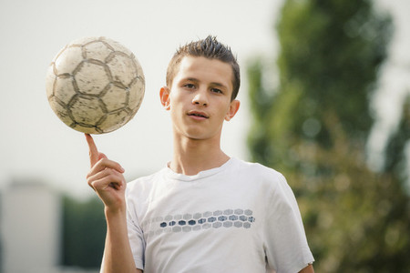 Portrait cool teenage boy spinning soccer ball on finger
