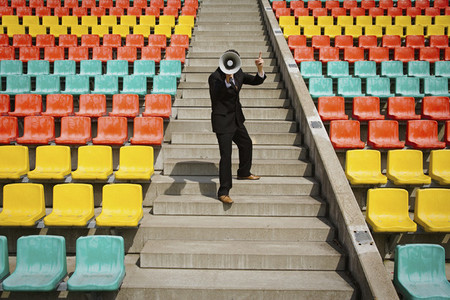 Businessman with bullhorn on sunny steps in stadium