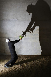 Man offering flowers to tall ominous shadow on wall