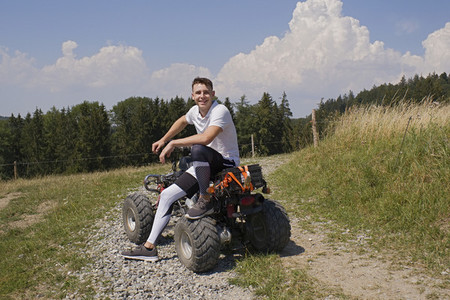 Portrait happy teenage boy on quadbike on sunny rural gravel road