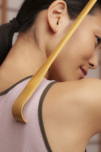 Close up young woman using wooden back scratcher