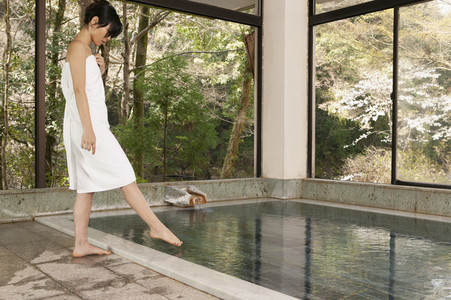 Young woman in towel dipping toe in water at Onsen