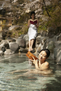 Young women relaxing and reading at sunny Onsen pool