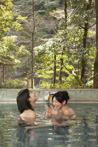 Happy young women friends soaking in pool at Onsen