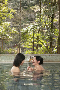Happy young women friends laughing in soaking pool at Onsen