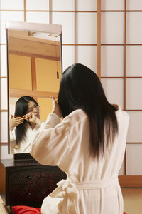 Young woman in bathrobe combing hair at mirror in spa