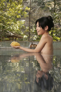 Beautiful young woman with loofah in hot spring water at Onsen
