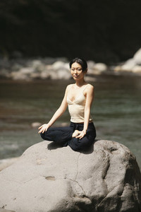 Portrait beautiful young woman meditating in lotus pose on sunny rock