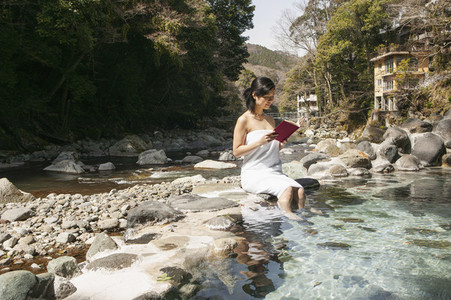 Young woman in towel reading book at sunny pool at Onsen Izu Japan