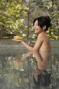 Happy young woman with loofah sponge in pool at Onsen