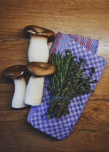 Fresh king oyster mushrooms and herbs on kitchen towel on wood table
