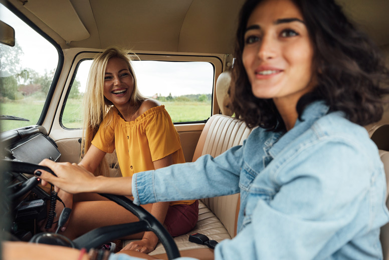 Smiling blond woman on a passenger seat looking at her friend while traveling by a van