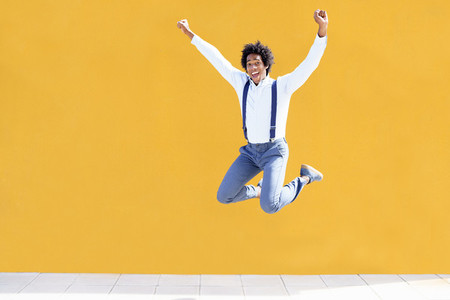 Black man with afro hair jumping on a yellow urban background