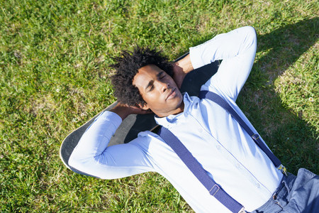Black businessman resting lying on the grass with his skateboard