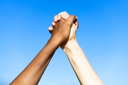 Multiethnic womens hands together against blue sky