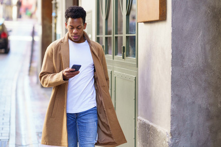 Young black man consulting his phone while walking down the street