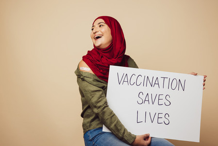 Cheerful muslim woman with banner of Vaccination saves lives