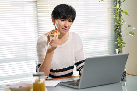 Woman eating some healthy food  while teleworking from home on her laptop