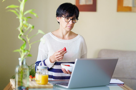 Woman eating strawberries while teleworking from home on her laptop