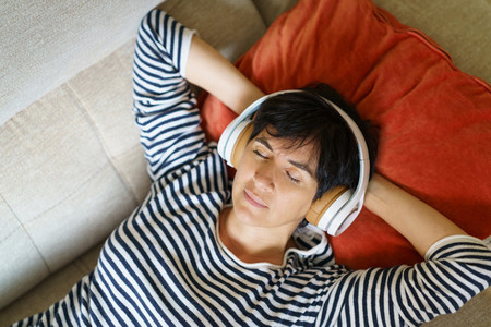 Middle aged woman listening to soothing music with headphones lying on her sofa