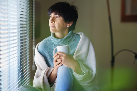Mid adult woman drinking coffee and looking out of the window in winter day