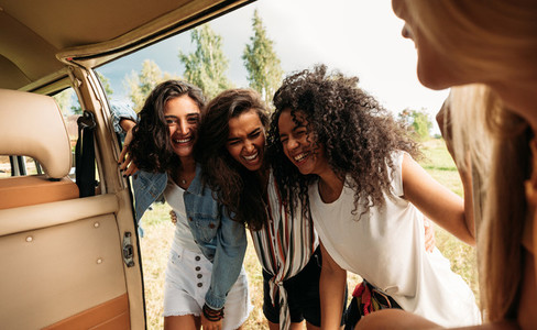 Group of friends on road trip laughing at van  Young people standing together and having fun at minivan door