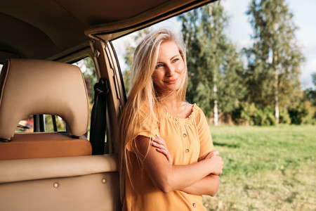 Beautiful blond woman with long hair leaning a van looking away