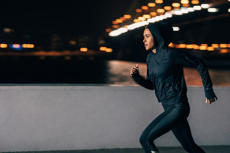 Side view of a woman in hoodie running at night  Middle east female jogger exercising outdoors