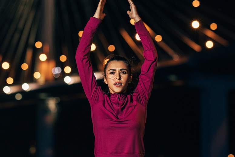 Female athlete in front of bridge at night. Woman wearing sportswear warming up body in the city in the evening.