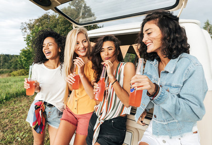 Group of four female friends celebrating during road trip standing at minivan