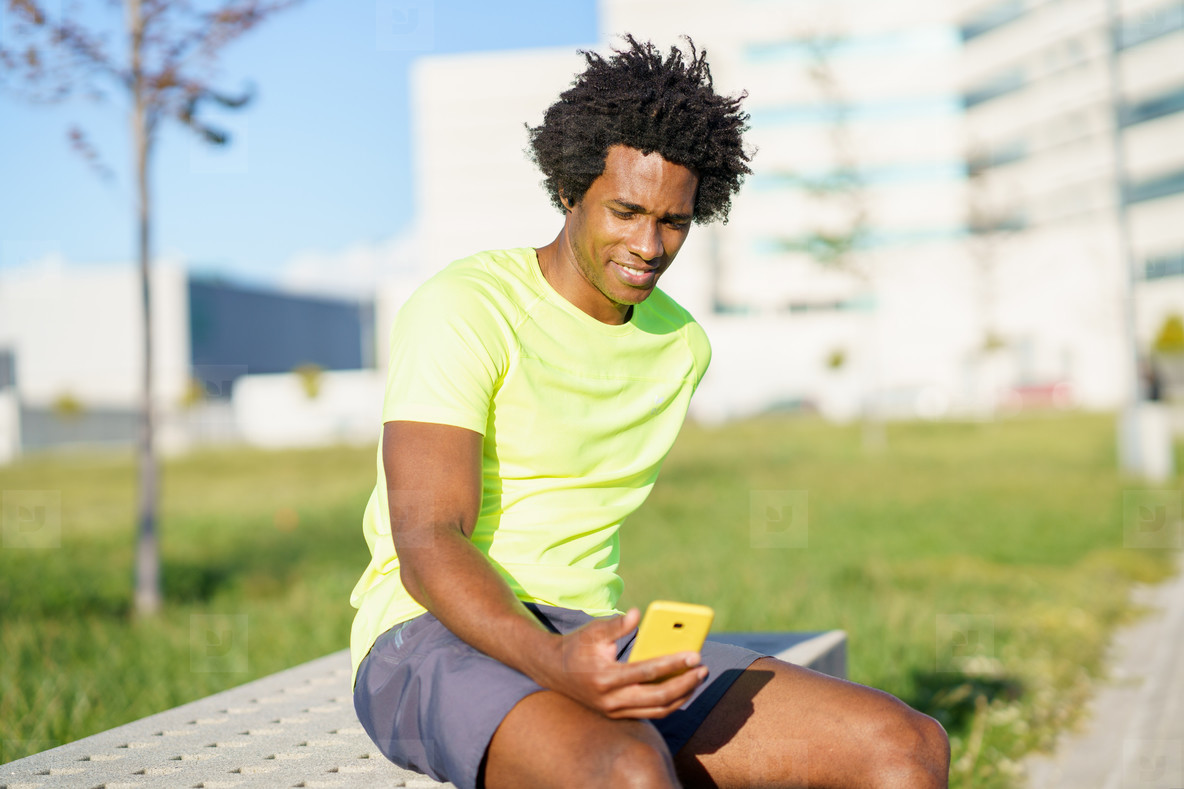 Black man consulting his smartphone with some exercise app while resting from his workout.