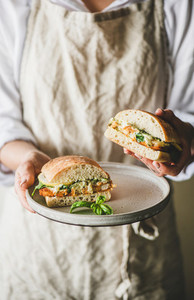 Woman holding fresh breakfast sandwich with fried fish lemon arugula