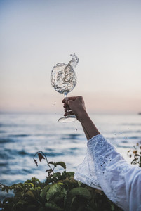 Woman holding glass of white flowing wine with sea background