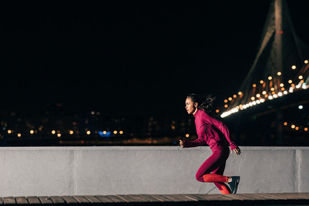 Woman runner at night  Sportswoman sprinting outdoors against a bridge