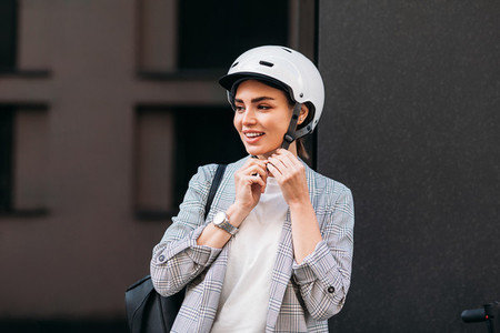 Young smiling woman fasten safety helmet on her head Businesswoman preparing for a ride on electrical scooter