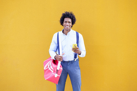 Black man with afro hairstyle carrying a sports bag and smartphone in yellow background