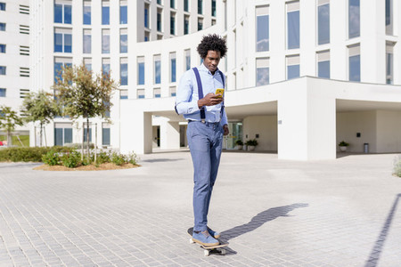 Black businessman on a skateboard looking at his smartphone outdoors