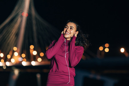 Cheerful woman in sport clothes enjoying music while standing at night