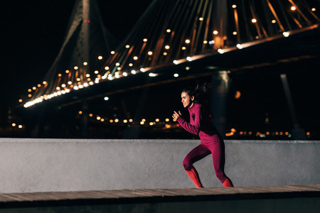 Female runner in sportswear exercising at night  Side view of a woman jogging outdoors at embankment