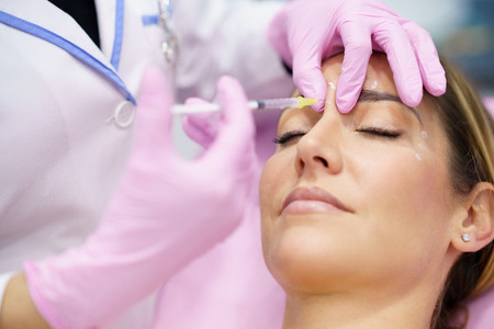Aesthetic doctor injecting botulinum toxin into the forehead of her middle aged patient