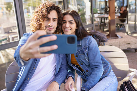 Arab couple taking selfie pictures with their smartphone  sitting on the terrace of a bar