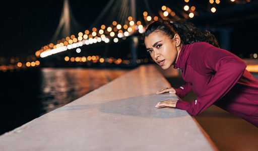 Young mixed race female athlete doing push ups on an embankment at evening