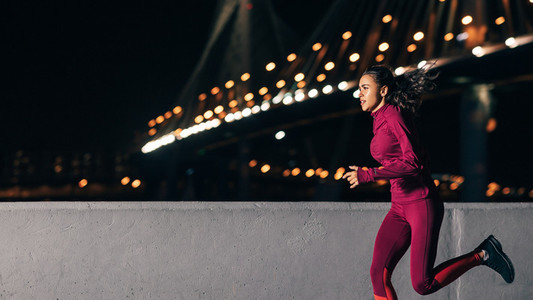 Mixed race woman in sports clothes running at night outdoors