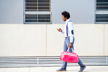 Black man with afro hairstyle carrying a sports bag and smartphone outdoors