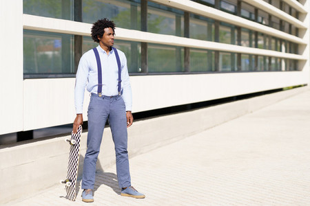 Black male worker standing next to an office building with a skateboard