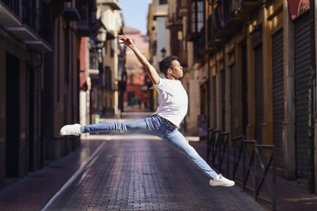 Young black man doing an acrobatic jump in the middle of the street