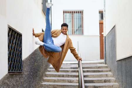 Young black man jumping for joy over a handrail in the street