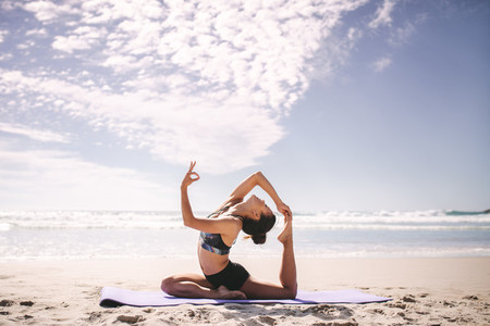 Woman doing one legged king pigeon pose on the beach